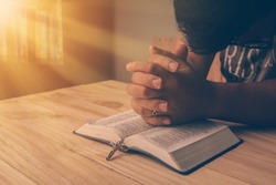 Christian hand while praying and worship for christian religion with blurred of her body background, Casual man praying with her hands together over a closed Bible. christian background. freedom.