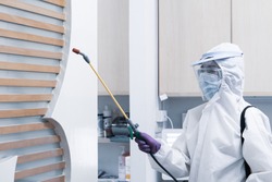 worker from decontamination services wearing personal protective equipment or ppe including white suit mask and face shield spraying disinfectant to cleaning coronavirus infection