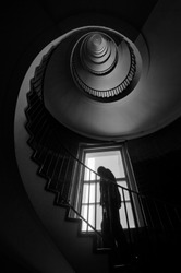 The silhouette of a man climbing the spiral staircase, dark black and white interior photography