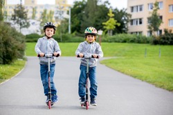 Two children, brothres, riding scooters in the park on a sunny autumn day, family activities during weekends
