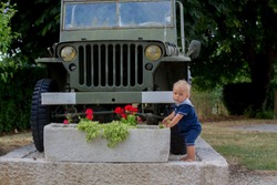Toddler boy, standing in front of old military autentic jeep car, summertime