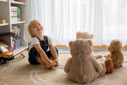 Little toddler boy, reading a book to his teddy bear friends at home, sitting in living room