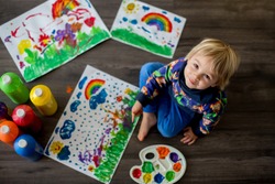 Sweet toddler blond child, boy, painting with colors, making finger prints on the paper