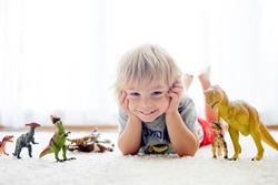 Blond toddler child, playing with dinosaurs at home, nice soft baclk light