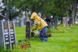 Sad little child, blond boy, standing in the rain on cemetery, sad person, mourning, summer rainy day