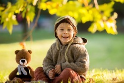 Little toddler child, boy, playing with knitted teddy bear in autumn park on sunset