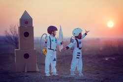 Two adorable children, boy brothers, playing in park on sunset, dressed like astronauts, imagining they are flying on the moon