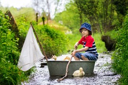 Cute child, boy, playing with boat and ducks on a little river, sailing and boating. Kid having fun, childhood happiness concept