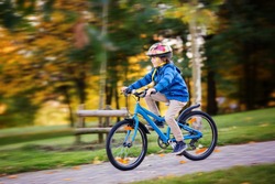 Cute child, boy riding bike in park, autumn afternoon soft sun light, blur motion