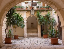 Beautiful backyard with arch, plants in pots, stairs and lantern. Patio decoration. Ancient courtyard background. Medieval architecture. Cozy italian backyard. Travel and architecture concept.