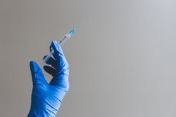 Hand in blue glove holding syringe with copy space. Syringe with sharp needle in hand. Medical treatment concept. Laboratory backgrouund. Medicare concept. Vaccination concept. 