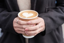 Woman hands holding Hot coffee paper cup, heart shape latte coffee art. Love, holiday, Valentine day and free plastic container concept