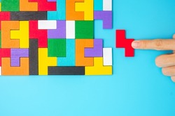 Hand connecting colorful wood puzzle pieces on blue background, geometric shape block. Concepts of logical thinking, Conundrum, solutions, rational, strategy, world logic day and Education