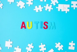 AUTISM text with white puzzle jigsaw pieces on blue background. Concepts of health, Autistic Spectrum disorder and world Autism awareness day