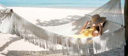 Happy Woman Traveler is relaxing in a hammock on the paradise beach. Female tourist in yellow dress rest near tropical sea. vacation, travel, summer, Wanderlust and holiday concept