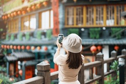 woman traveler visiting in Taiwan, Tourist taking photo and sightseeing in Jiufen Old Street village with Tea House background. landmark and popular attractions near Taipei city. Travel concept