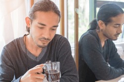 Handsome Asian man portrait with long hair tied up, holding a black coffee mug. He looked at the coffee cup with the light shining from behind, showing a straight expression. 