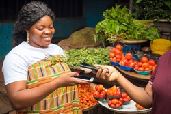 african woman in a market receiving payment via contactless transfer of funds from a customer using their mobile phones