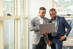 young black business men standing together holding a laptop, discussing business