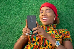 a beautiful african lady laying on the floor in a park using her mobile phone
