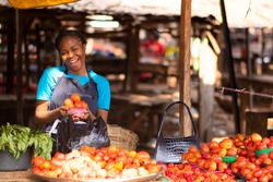 happy nigerian trader in a local market holding a bowl of tomatoes
