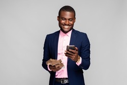 young african businessman wearing a suit, holding a lot of money and using his phone