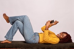 black lady lying on a bench using a phone rejoices