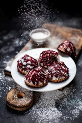 small desserts with different stuffing, sprinkled with berry topping, sprinkled with powdered sugar on a white plate on a wooden board, on a dark background