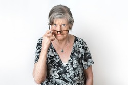 Portrait of blue-eyed angry senior woman peering over her eyeglasses on white background studio shot.