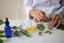 Scientist or doctor making  alternative medicine herb , mortar, laboratory glassware, plant in tube, flower , on white background. Hand focused.