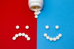 Pills smileys. Happy and sad smileys made of pills and a plastic bottle on a split blue and red background. Antidepressants experience. Healing process. Correct medication or right medical treatment.