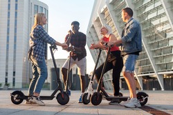 interracial group of young friends ride electric scooters in the city and communicate, multiracial young people use electric vehicles and talk