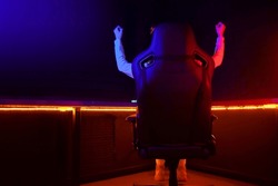 gamer plays a computer game at night and celebrates a victory, the player sits in a comfortable computer chair with his hands up, victory gesture