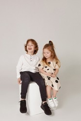 Cute stylish children on studio background. Two beautiful teens, girl and boy sitting together. Stylish toddler girl posing with cute teen boy at the studio. Siblings day. Kids fashion concept