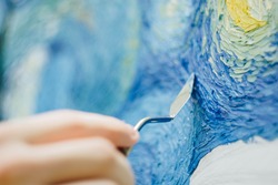 the hand of a European artist holds a mastekhin smeared in oil paint and draws a picture. Van Gogh's replica Starry night. blurred background. Close-up.
