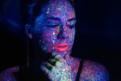 Fashion model woman in neon light, portrait of a beautiful model with fluorescent makeup, body art design in UV, painted face, colorful makeup, on a black background of a girl. Disco dancer in neon 