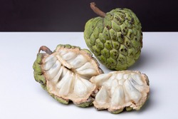 Top down view of opened up and intact Sugar-apple or 'Fruta de Conde' [Earl Fruit] as it is known in Brazil on a white surface with dark background showing inside with fleshy 'teeth' and outside peel