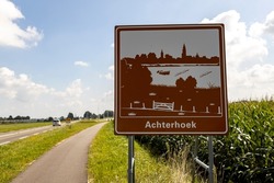 Curved bike road next to freeway with traffic sign orienting entrance of the province area Achterhoek against a blue sky with clouds in countryroad with corn field on the side
