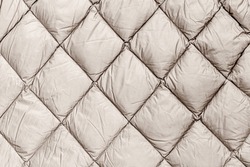 Quilted fabric backdrop. Beige quilt texture blanket or puffer jacket. Warm winter jacket with modern quilted pattern for cold winter season. Down jacket fashion background. 