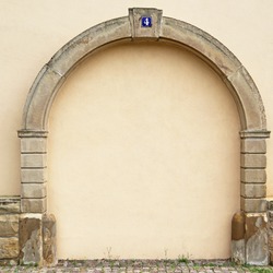 The walled-up door with stone arch with metal rusty blue table with white number four on the ancient beige plastered walls background, photo frame, place for text