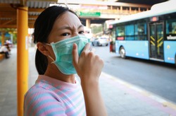 Tired asian child girl cough wearing hygienic mask,stressed worried about air pollution problems,toxic fumes,PM 2.5,dust,bad environment at bus stop in city,protect their health from smog,Covid-19