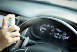 Hand of woman is spraying alcohol,disinfectant spray on steering wheel in her car,prevent infection of Covid-19 virus,contamination of germs or bacteria,wipe clean surfaces that are frequently touched