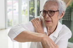 Asian senior woman massage her shoulder bone with hand,aching and tingling,old elderly patient with frozen shoulder,pain and stiffness in the shoulder,degenerative disease,rheumatoid arthritis or gout