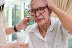 Closeup,glass of water with ice,senior grandmother with a brain freeze after drinking cold water,severe pain in her head,Asian elderly woman getting brain freeze,health care,food and drinks concept