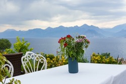 Bouquet of flowers on the table in outdoor cafe with sea and mountains view. Blurred background.