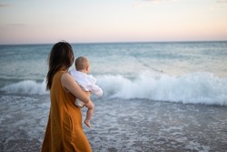 Mom holds her son in her arms. Mother and the child meets the sunset on the sea. pastime of mom and son. Happy motherhood. Mom and son relationship.