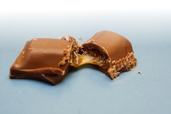 Delicious gooey, sticky caramel toffee seeping out from a broken chocolate bar with crumbs.