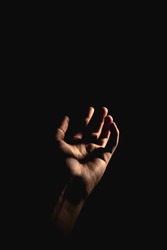Hand with light and shadows reaching out against a dark background