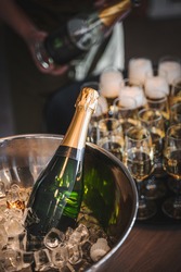 bottle of champagne in ice and person pouring glasses in the background
