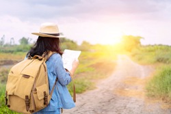 Female tourists are using a map to find the direction of a place. The road is a long way. An adventure trip by yourself with a backpack in the back